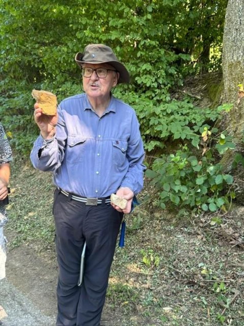 Ein Mann mit Hut zeigt einen Stein im Wald